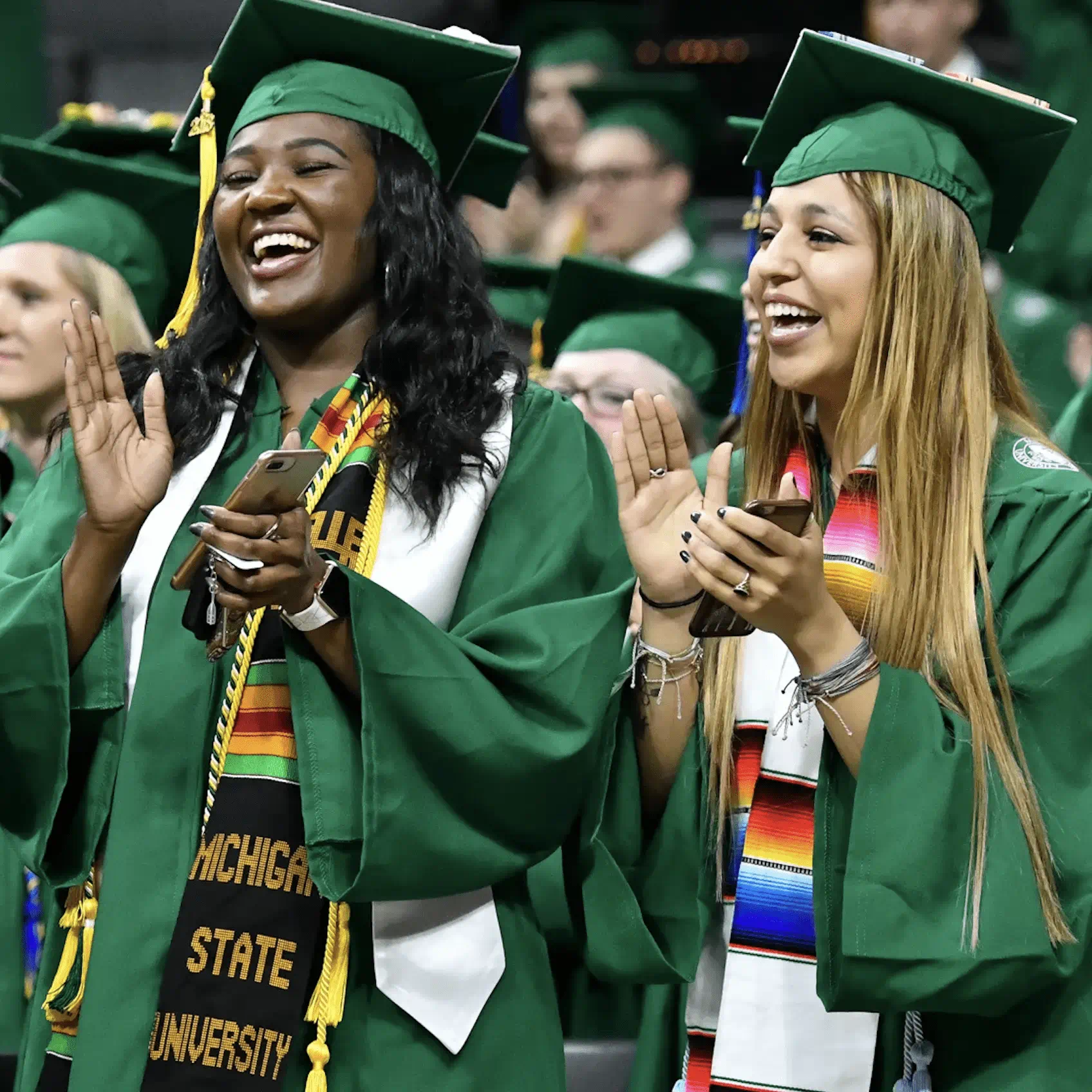 Graduates in green gowns and caps clapping